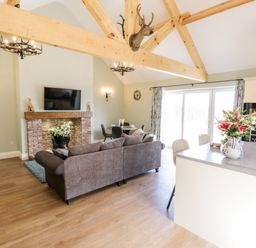 A living room with a gray sofa and mounted TV above brick fireplace with flowers on hearth at Stag Cottage at Broadings Farm in Whitby