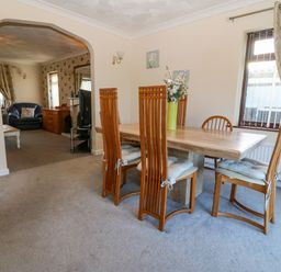 A dining area with wooden chairs and a table with a vase of flowers next to a window with curtains at Rhiangwyn in Llanrhyddlad near Cemaes Bay