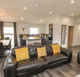 An open plan living room and kitchen with black leather sofas yellow cushions dining table and chairs and kitchen island at Box Tree Escapes in Kirkby Lonsdale