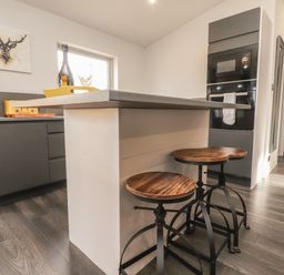 A kitchen with a countertop island and three wooden stools with black metal legs at Box Tree Escapes in Kirkby Lonsdale