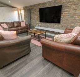 A living room with three brown leather sofas pink cushions a wooden coffee table and a wall mounted tv at Box Tree Escapes in Wennington near Kirkby Lonsdale