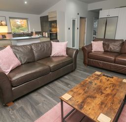 A living area with two brown leather sofas with pink cushions and a wooden coffee table at Box Tree Escapes in Wennington near Kirkby Lonsdale