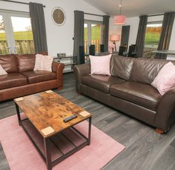 A living room with two leather sofas a wooden coffee table a pink rug and dining area visible at Box Tree Escapes Wennington near Kirkby Lonsdale