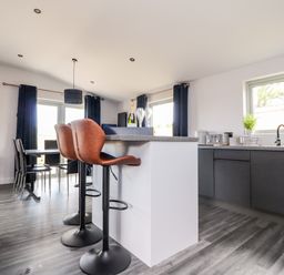 A kitchen and dining area with bar stools and a clock on the wall at Box Tree Escapes Wennington near Kirkby Lonsdale