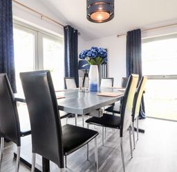 A dining room with a black table and black chairs a vase with flowers and dark curtains at Box Tree Escapes Wennington near Kirkby Lonsdale