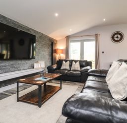 A living room with two black leather sofas a wooden coffee table and a wall mounted television at Box Tree Escapes in Wennington near Kirkby Lonsdale