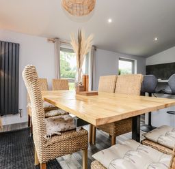 A dining area with a wooden table and woven chairs with cushions and a vase with dried plants on the table at Box Tree Escapes in Wennington near Kirkby Lonsdale