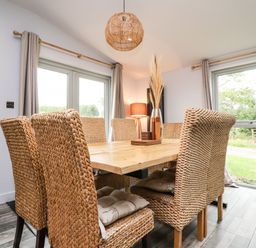 A dining room with wicker chairs and a wooden table by windows at Box Tree Escapes Wennington near Kirkby Lonsdale