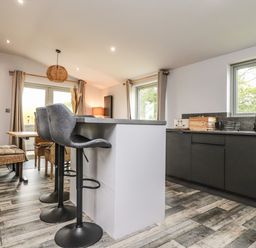 A kitchen with a breakfast bar and stools dining table and chairs and windows at Box Tree Escapes in Wennington near Kirkby Lonsdale