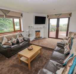A living room with brown leather sofas a coffee table a white brick fireplace and large windows at Oakland Cottage in Summerhill near Saundersfoot
