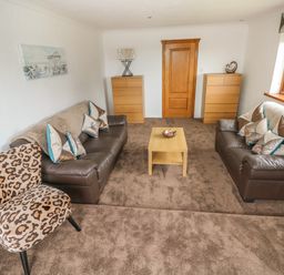A living room with two brown sofas a leopard print chair a wooden coffee table and two wooden dressers at Oakland Cottage in Summerhill near Saundersfoot
