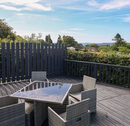 An outdoor deck with a glass top table and four wicker chairs surrounded by a railing and greenery at Oakland Cottage in Summerhill near Saundersfoot