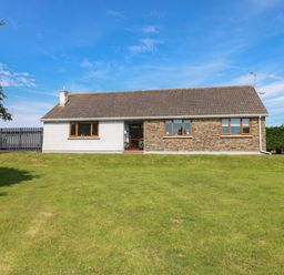 A single-story house with a mixed stone and white exterior and a large grassy lawn at Oakland Cottage in Summerhill near Saundersfoot