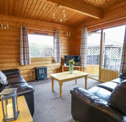 A living room with two leather sofas a wooden coffee table with flowers a TV and windows with curtains at Valley View in Rhayader