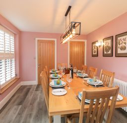 A dining room with a wooden table and chairs set with plates glasses and pears on napkins at Hazelnut Cottage in Windermere