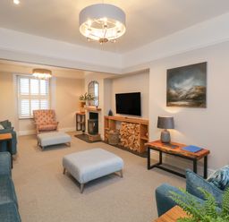 A living room with sofas armchair ottomans a TV and firewood at Hazelnut Cottage in Windermere