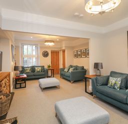 A living room with blue sofas, wooden side tables with lamps, two ottomans, a wall clock, and a TV at Hazelnut Cottage in Windermere