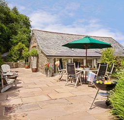An outdoor patio with chairs table umbrella and barbecue near a stone building at Garden House in Cornworthy