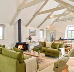 A living room with green sofas a wooden coffee table a fireplace and a kitchen area at Garden House in Cornworthy