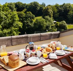 An outdoor wooden table set for breakfast with bread croissants orange juice and yogurt glasses at Haytor Cottage Cornworthy
