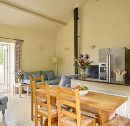 An open kitchen and dining area with wooden table and chairs blue sofas and a stainless steel refrigerator at Haytor Cottage in Cornworthy