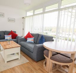 A living room with two grey sofas a wooden coffee table a round dining table with chairs and large windows with vertical blinds at Pebbles in Cromer