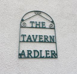 A metal sign on a textured wall reading The Tavern Ardler