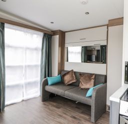 A living room with a gray sofa with cushions near a window and a kitchen stove at Cabin at the Tavern in Coupar Angus
