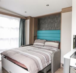 A bedroom with a double bed next to a window and a kitchen counter with stove at Cabin at the Tavern in Coupar Angus