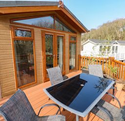 An outdoor deck with a glass table and four chairs next to a wooden cabin with large windows and a door at Jules @ 79 Stepaside