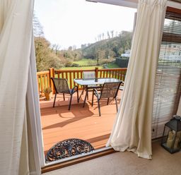 A view through a sliding door to a wooden deck with table and chairs and a grassy landscape beyond at Jules @ 79 in Stepaside