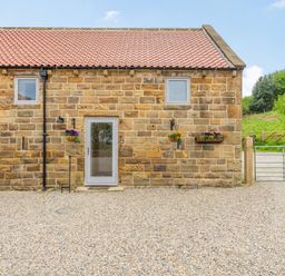 A stone building with two small windows a glass door hanging flower baskets gravel ground and a metal gate at Meadowsweet in Goathland