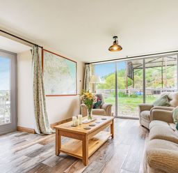 A living room with a wooden coffee table candles and flowers two armchairs and a sofa with cushions a large map on the wall glass sliding doors and a door leading outside at Meadowsweet in Goathland