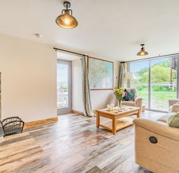 A living room with two armchairs a coffee table with flowers and candles a wood stove and large windows showing greenery outside at Meadowsweet in Goathland