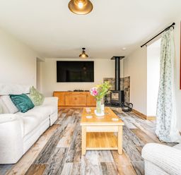 A living room with a beige sofa with cushions a wooden coffee table flowers a wall-mounted television a wooden cabinet a wood-burning stove and a curtain with a map at Meadowsweet Goathland