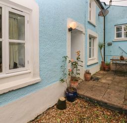 A small courtyard with blue walls and white framed windows with potted plants and a bench at Pant y FFynnon in St Davids