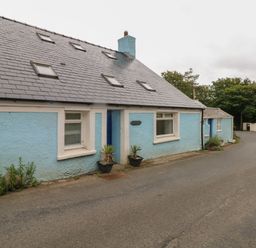 A blue painted house with small windows and a sloped roof beside a paved road at Pant y FFynnon in St Davids