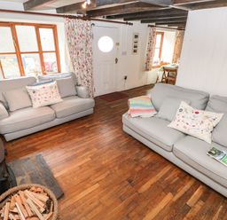 A living room with two sofas a basket of firewood and wooden floors at Pant y FFynnon in St Davids