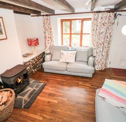 A living room with a wood stove fire a basket of firewood two sofas wood floors and a window at Pant y FFynnon in St Davids