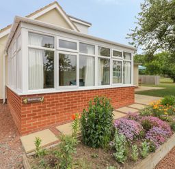 A patio garden with flowers and shrubs next to a brick conservatory at Buttercups at Midway in Kington