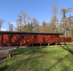 A red wooden cabin with a wooden deck and stairs surrounded by grass and trees at Great Leap in Louth