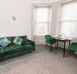 A living room with a green sofa two green chairs a black table and two framed pictures on the wall at Emerald Suite in Barmouth