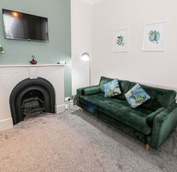 A living room with a green sofa and cushions near a fireplace with a TV mounted above it at Emerald Suite in Barmouth
