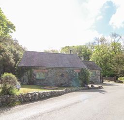 A stone cottage with green window frames surrounded by trees and a stone wall at Glyn Yr Efail in Moylegrove nr Newport and Cardigan