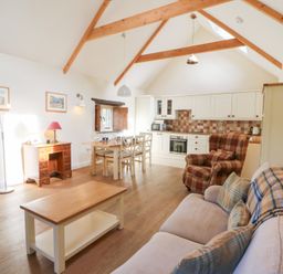 An open plan living room and kitchen with wooden beams a dining table and chairs a sofa and an armchair at Glyn Yr Efail in Moylegrove nr Newport and Cardigan