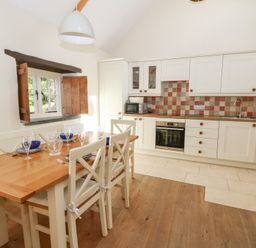 A kitchen with wooden table and white chairs next to cream cabinets and tiled backsplash at Glyn Yr Efail in Moylegrove nr Newport and Cardigan