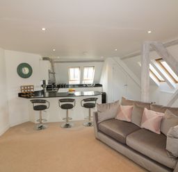An open plan room with a kitchen counter with three bar stools and a sofa with cushions at Stores & Supplies in Bodmin