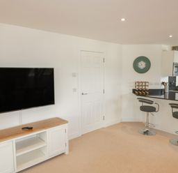 A room with a wall-mounted TV above a wooden cabinet a door and a kitchen counter with two bar stools at Stores & Supplies in Bodmin