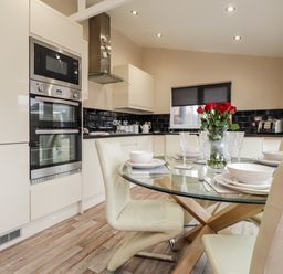 A kitchen with a glass dining table set with white dishes and red flowers at Sparrows Den Lodge in Winchelsea Beach