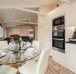 A kitchen and dining area with a glass table set with white dishes and a vase of red roses at Sparrows Den Lodge in Winchelsea Beach